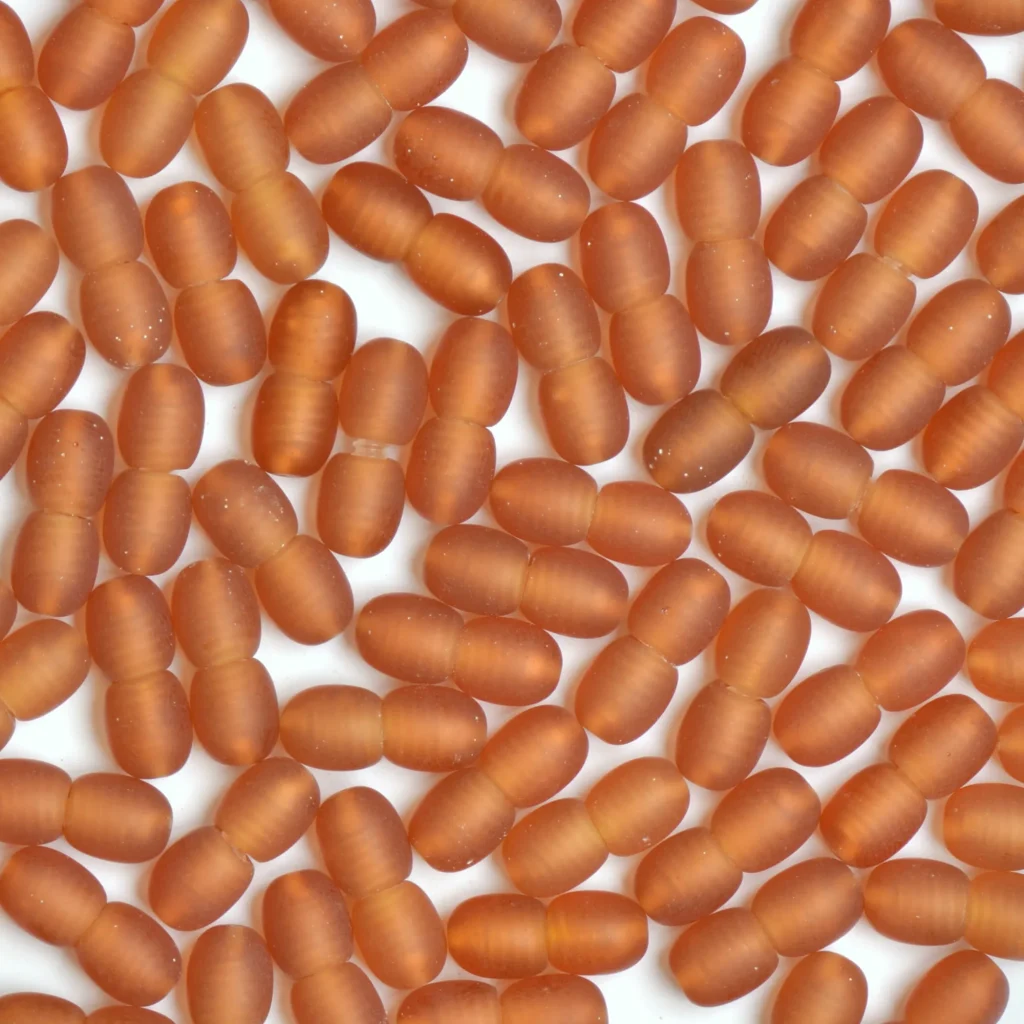 Close-up of orange capsule-shaped beads on a white background, showcasing smooth, matte finish and uniform shape.