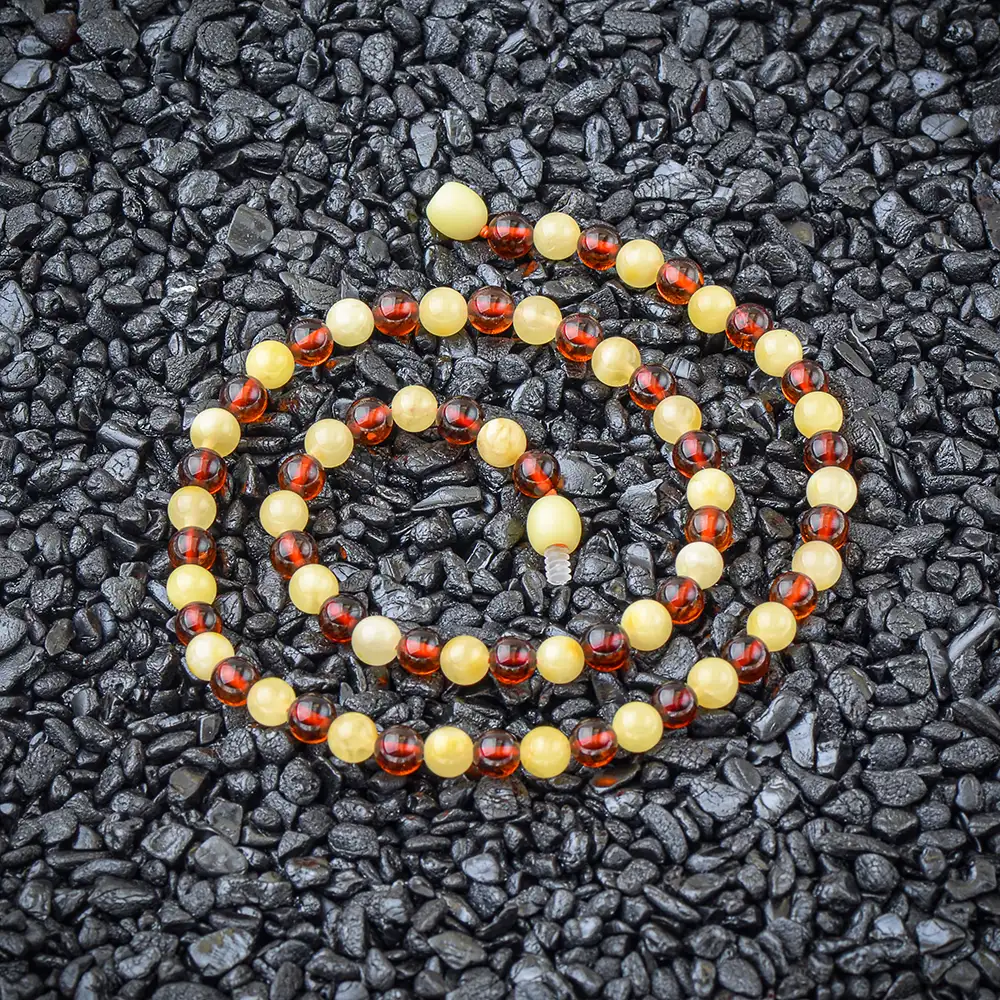 Colorful Baltic amber beaded necklace on black textured background, showcasing natural warmth and handcrafted elegance.