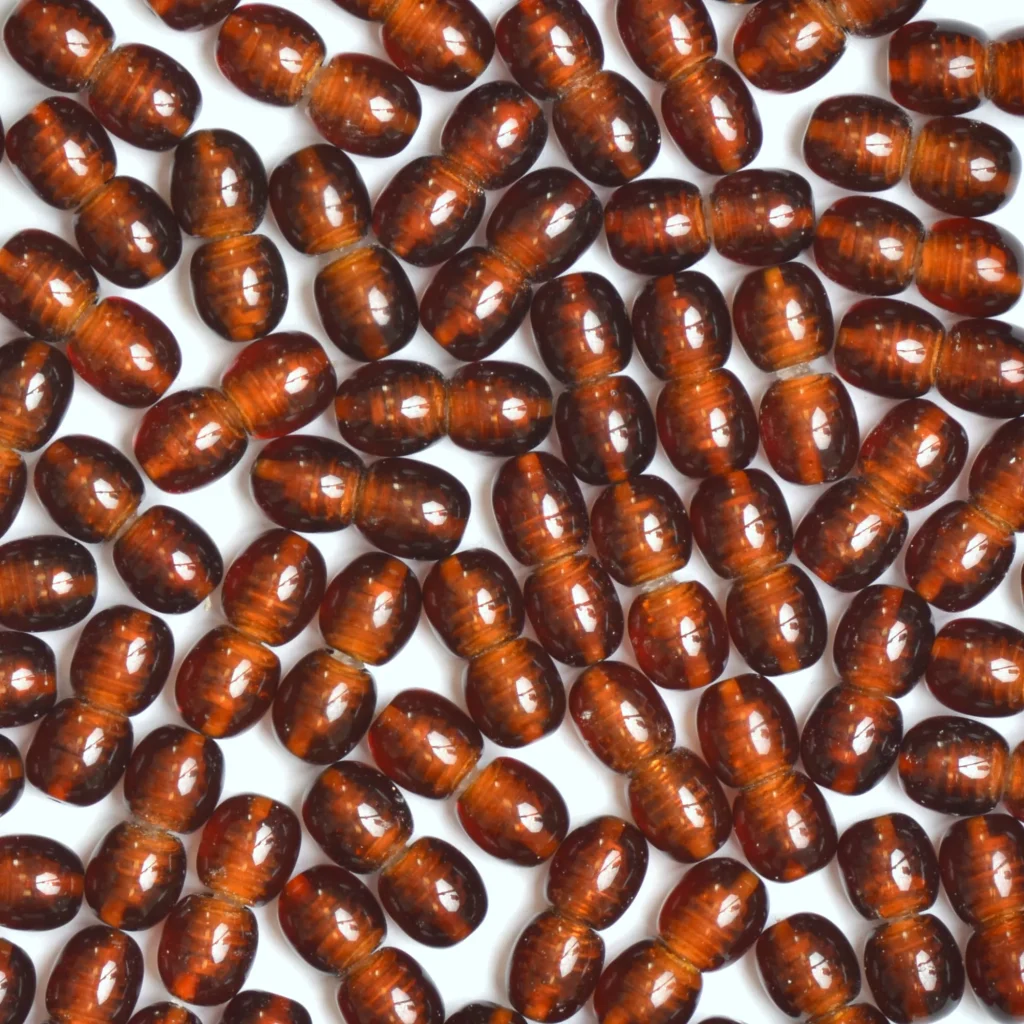 Close-up of glossy, reddish-brown oval amber beads for jewelry or decoration.