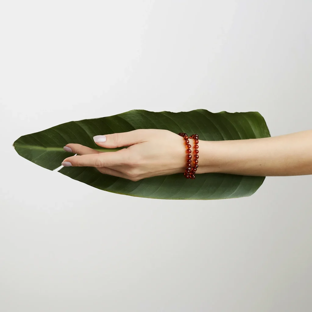 Hand holding vibrant green leaf with amber bracelet, symbolizing nature and elegance.