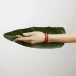 Hand holding vibrant green leaf with amber bracelet, symbolizing nature and elegance.