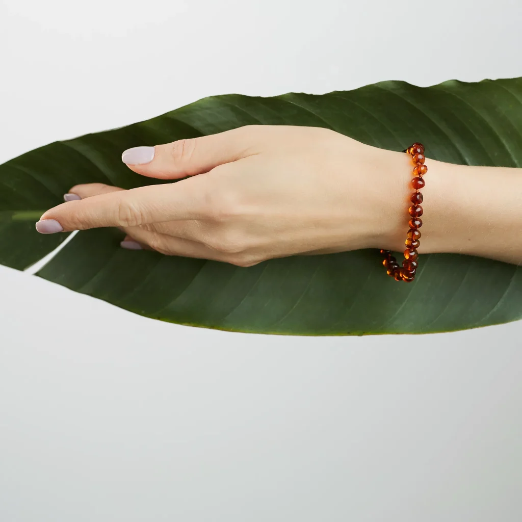 Hand resting on vibrant green leaf wearing a polished amber bracelet with subtle elegance.