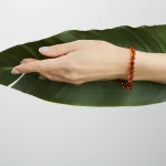 Hand resting on vibrant green leaf wearing a polished amber bracelet with subtle elegance.