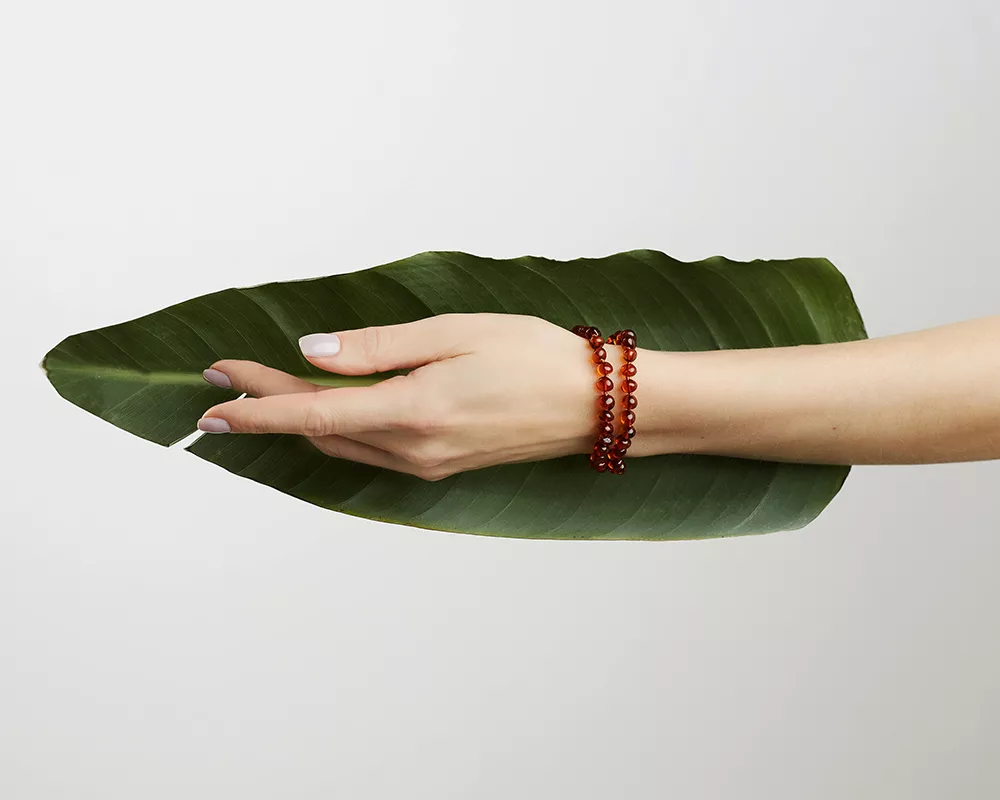 Amber as alternative medicine. Benefits to health. Picture of a green leaf and amber bracelets on a woman's hand