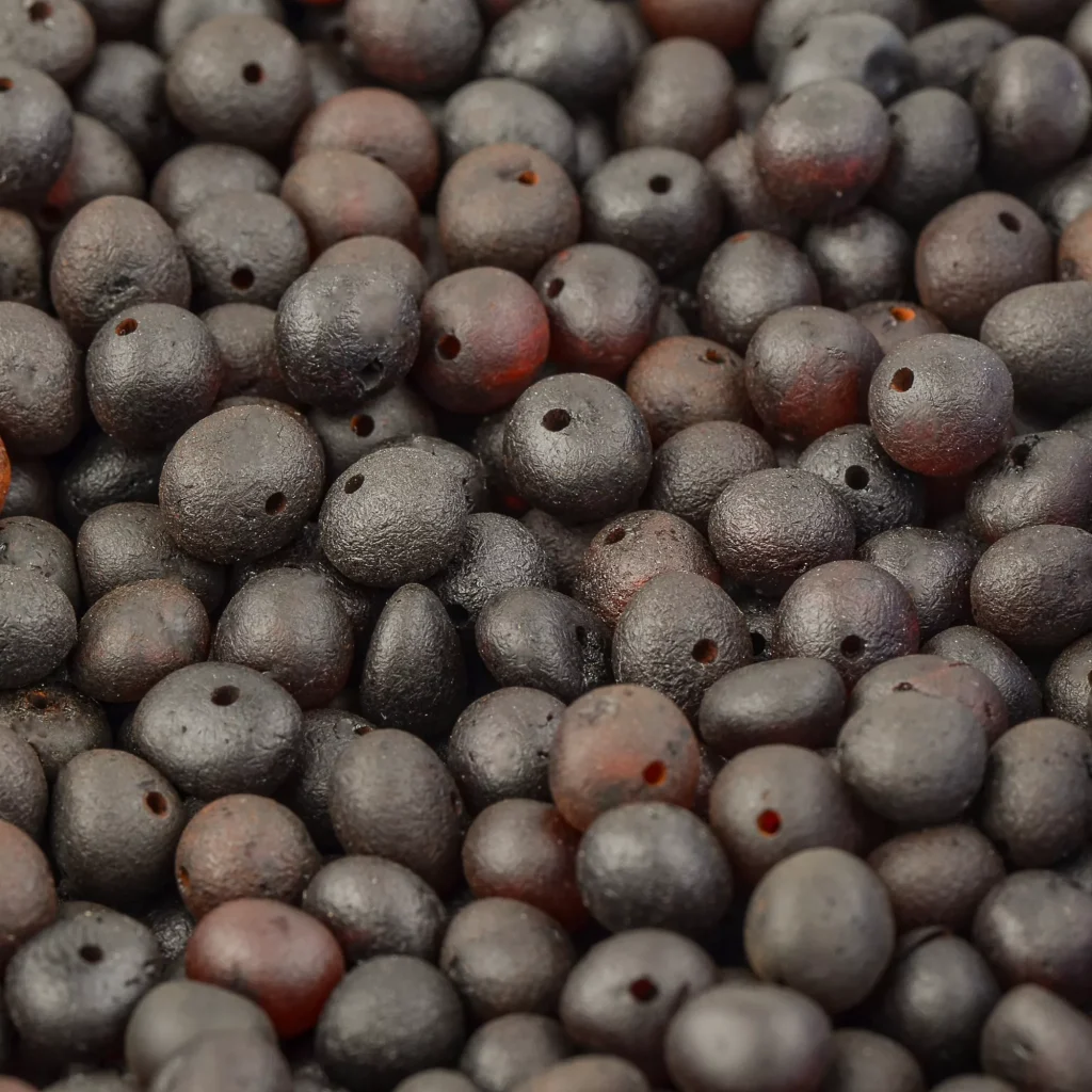 Close-up of dark organic seed beads with natural textures and subtle shimmer for jewelry making.