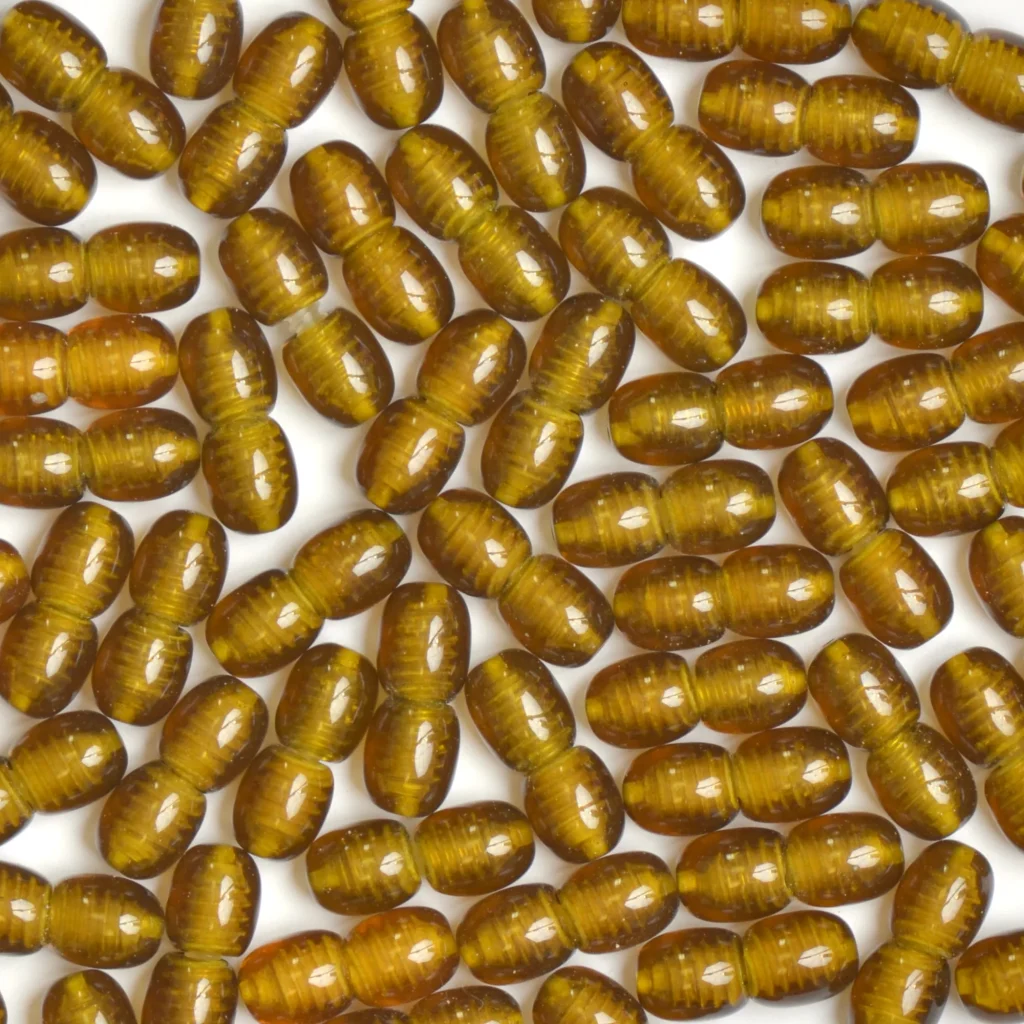 Close-up of shiny golden-brown capsules with smooth, ridged surfaces on a light background.