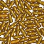 Close-up of shiny golden-brown capsules with smooth, ridged surfaces on a light background.