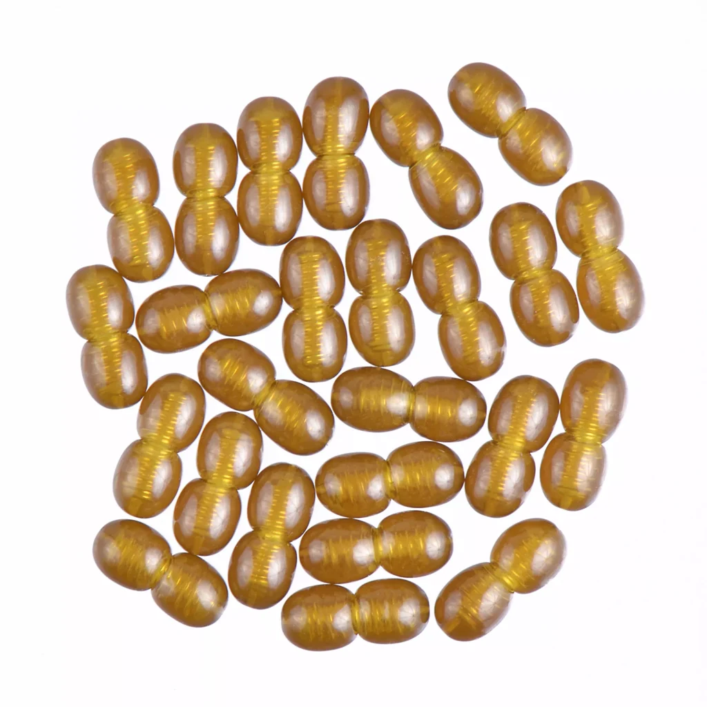 Golden oval capsules in a dense, shiny cluster with reflective, luxurious appearance.