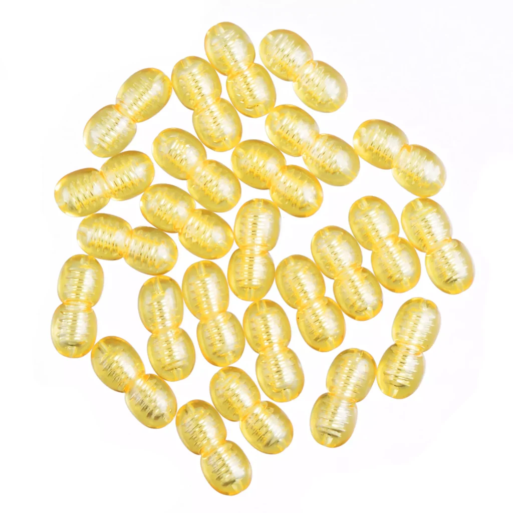 Collection of glossy yellow oval capsules with ribbed texture on white background.