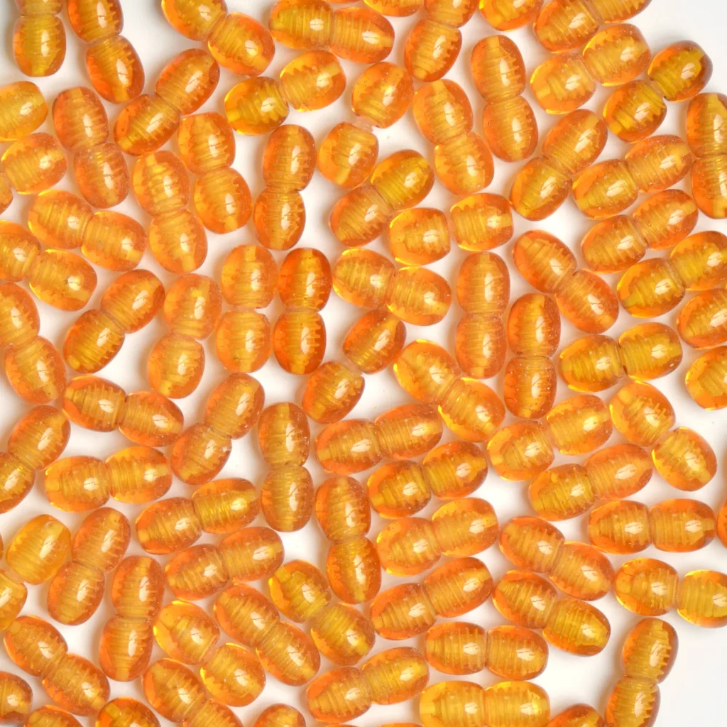 Close-up of vibrant orange seed-like beads with glossy, ribbed surfaces on white background.