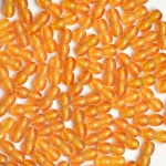 Close-up of vibrant orange seed-like beads with glossy, ribbed surfaces on white background.