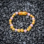Colorful beaded bracelet with pink, yellow beads on black stones background, elegant and vibrant accessory.