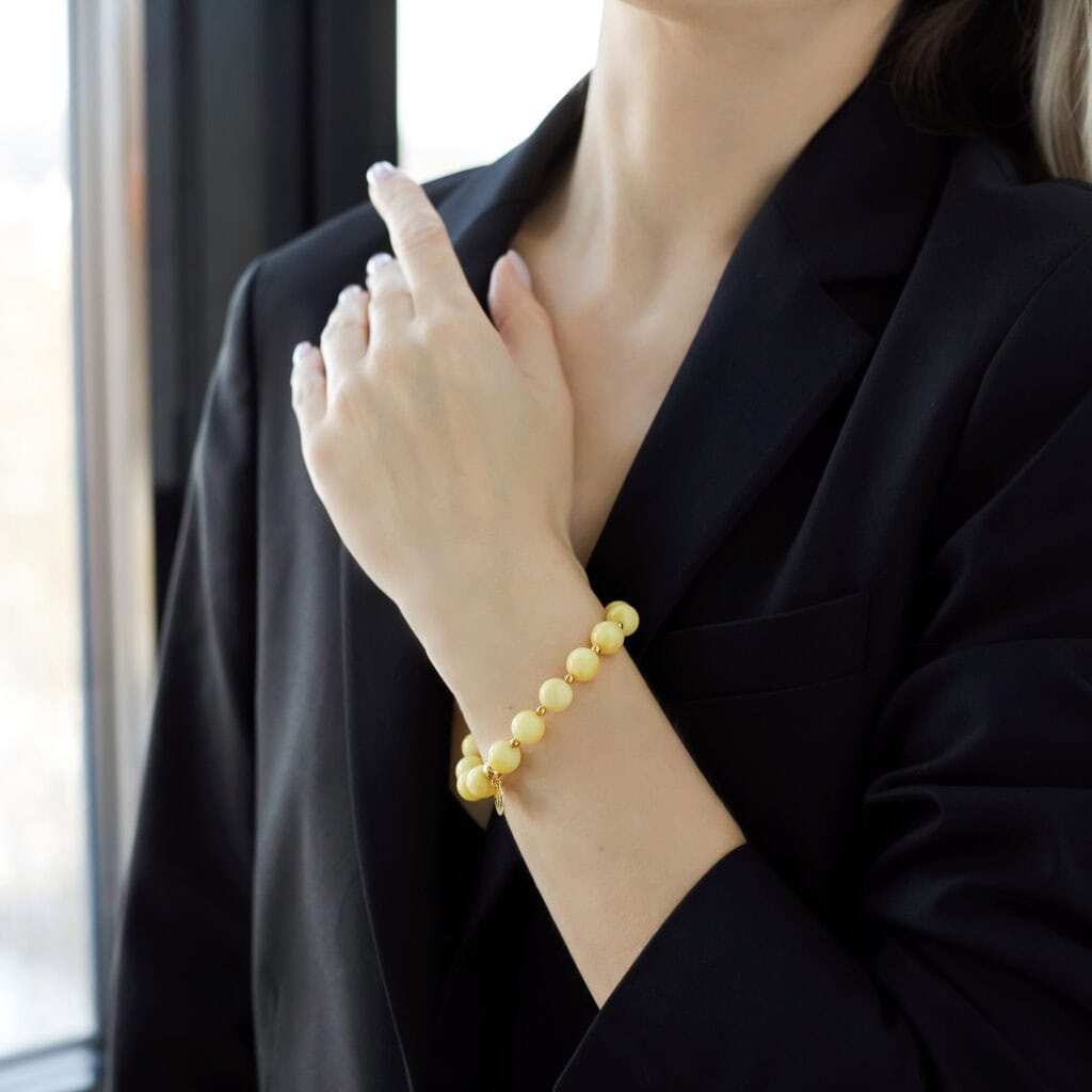 Stylish leather blazer with vibrant yellow beaded bracelet and manicured nails, natural light enhances elegance.