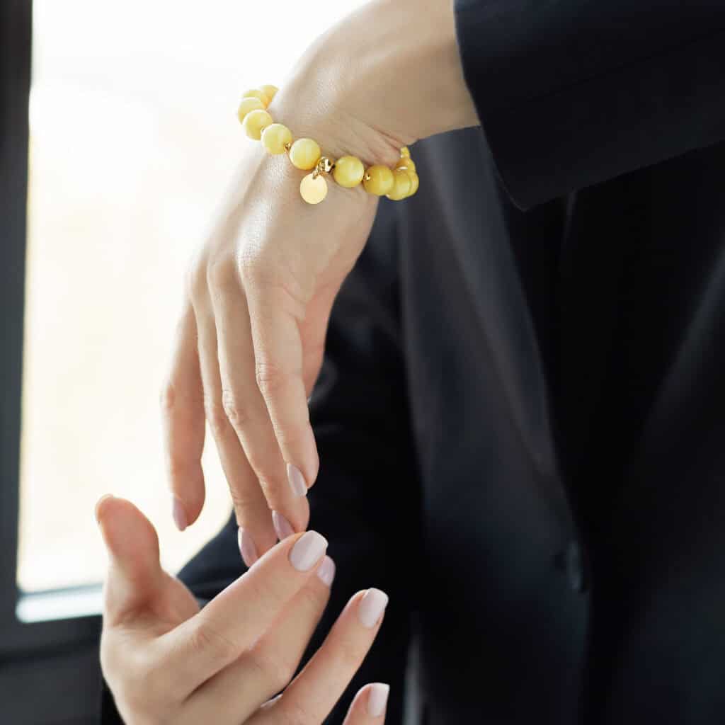 Elegant yellow beaded bracelet with charm on a womans hand in a tailored suit.