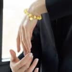 Elegant yellow beaded bracelet with charm on a womans hand in a tailored suit.