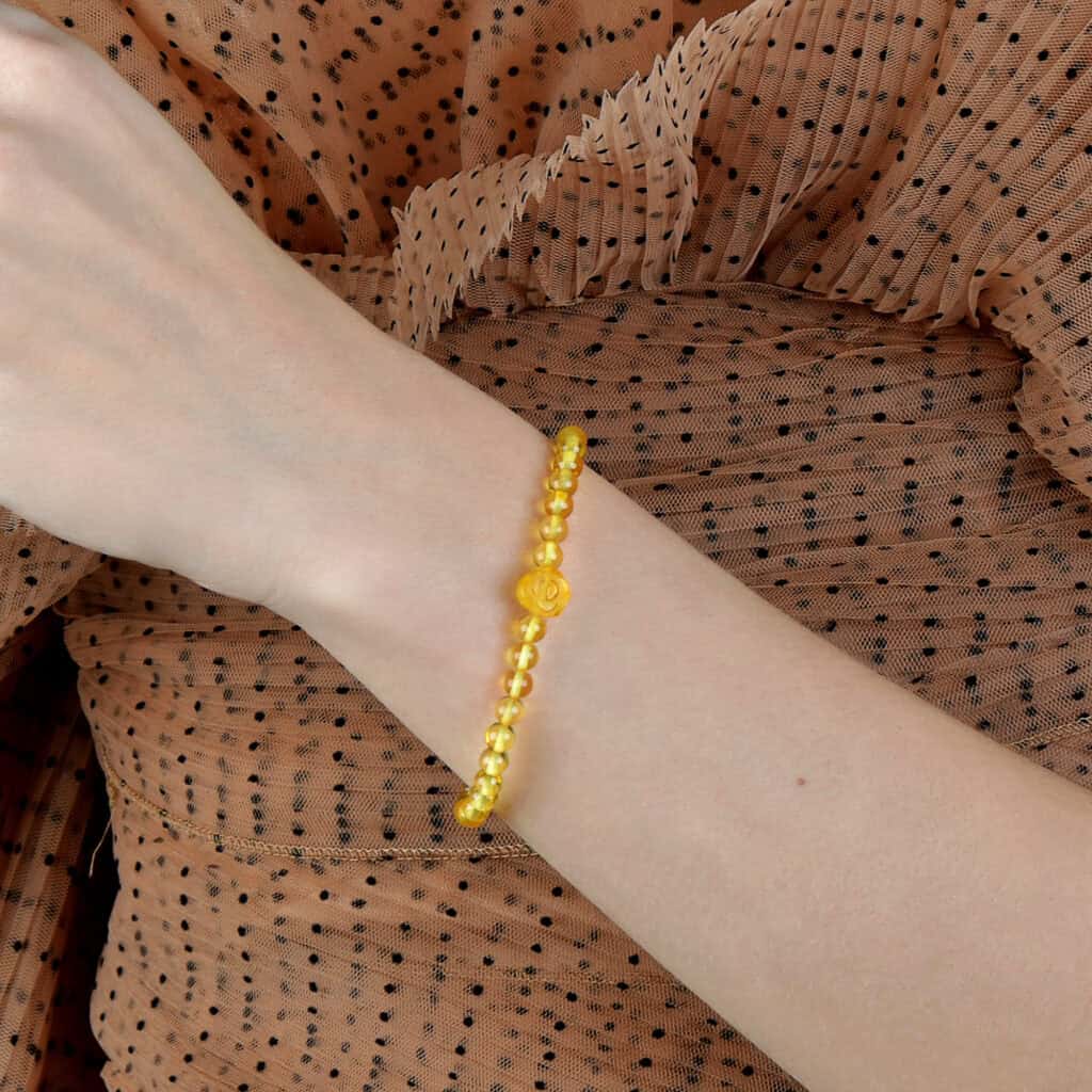 Bright yellow beaded bracelet with central bead on wrist, against polka dot fabric background.