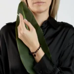 Elegant woman holding vibrant green leaf with beaded star bracelet and sleek black shirt.