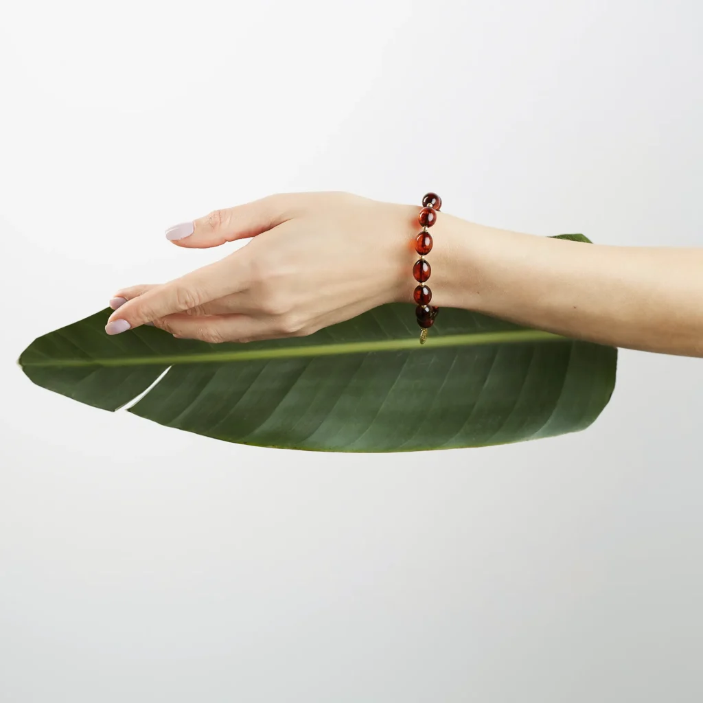 Close-up of hand with amber bracelet resting on vibrant green leaf, emphasizing natural elegance.