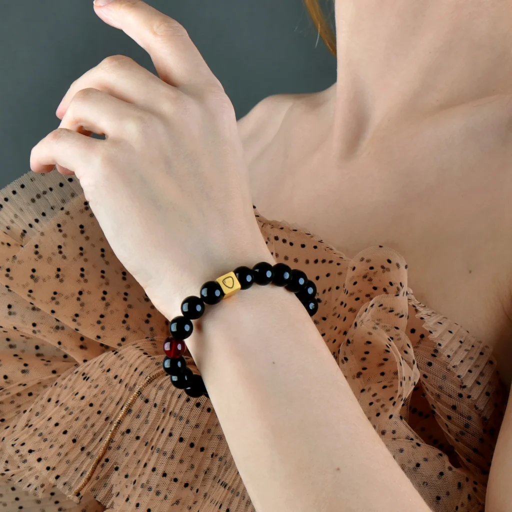 Elegant womans arm with black and red bead bracelet, sheer polka dot top, soft lighting, stylish accessory.