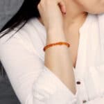 Elegant amber beaded bracelet on womans arm with white shirt and soft gray background.
