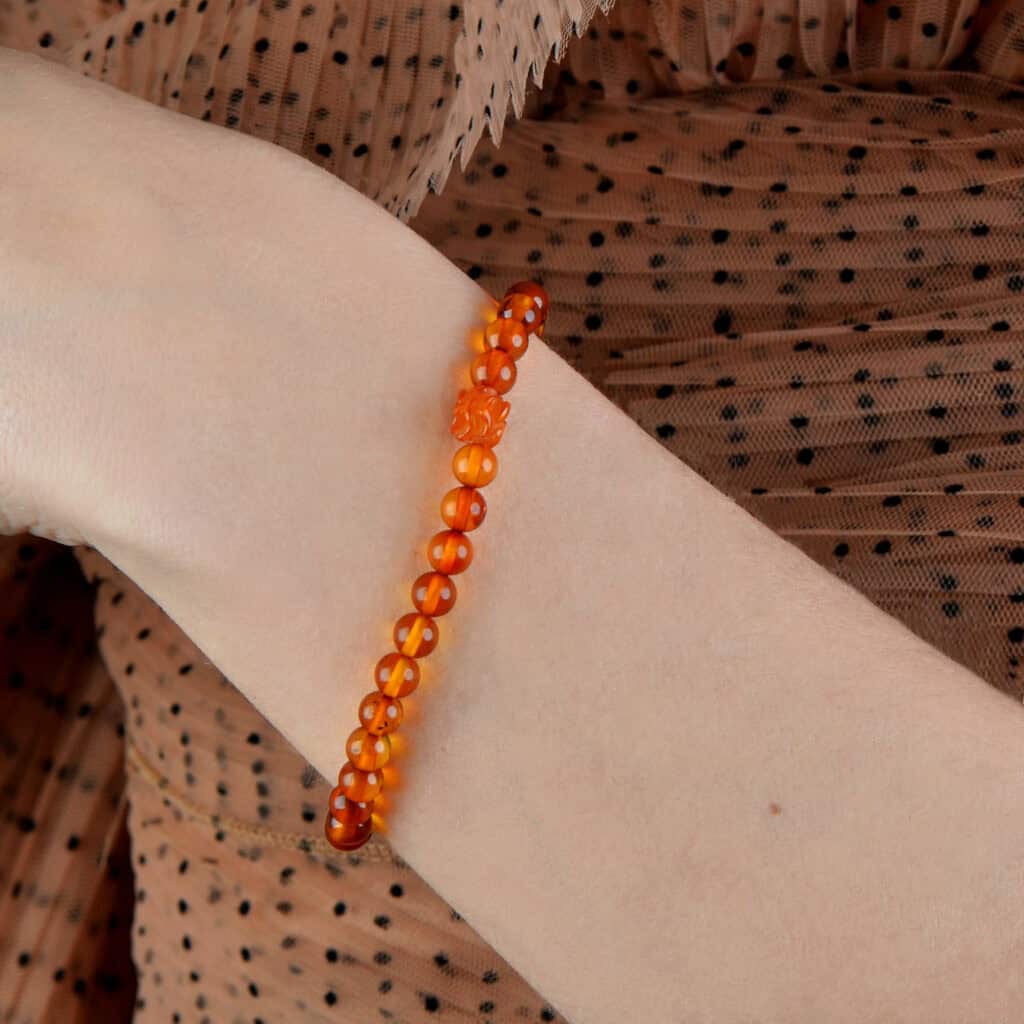 Colorful orange beaded bracelet on a wrist against polka dot fabric background.