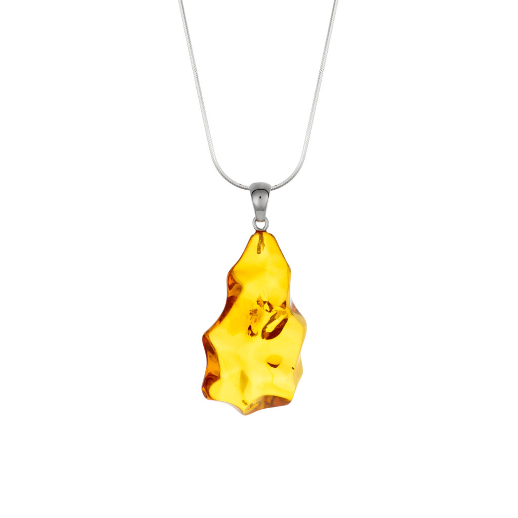 A close-up image of a genuine amber pendant showcasing its warm, golden hues. The amber is transparent with natural inclusions, capturing its organic beauty. The pendant is encased in a silver or gold frame, adding elegance to the raw, fossilized resin. The smooth surface of the amber reflects light, highlighting its natural glow and intricate details. This timeless piece of jewelry hangs delicately from a chain, blending nature and craftsmanship.