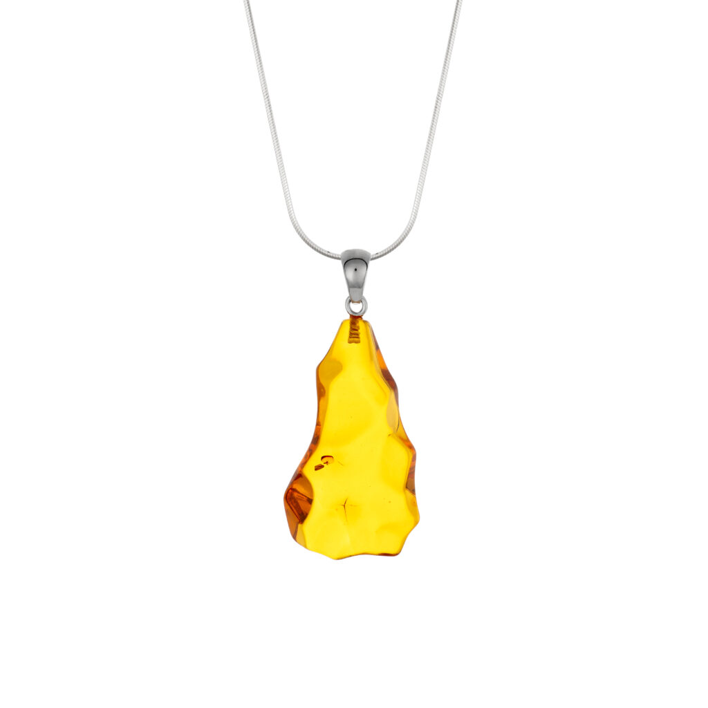 A close-up image of a genuine amber pendant showcasing its warm, golden hues. The amber is transparent with natural inclusions, capturing its organic beauty. The pendant is encased in a silver or gold frame, adding elegance to the raw, fossilized resin. The smooth surface of the amber reflects light, highlighting its natural glow and intricate details. This timeless piece of jewelry hangs delicately from a chain, blending nature and craftsmanship.