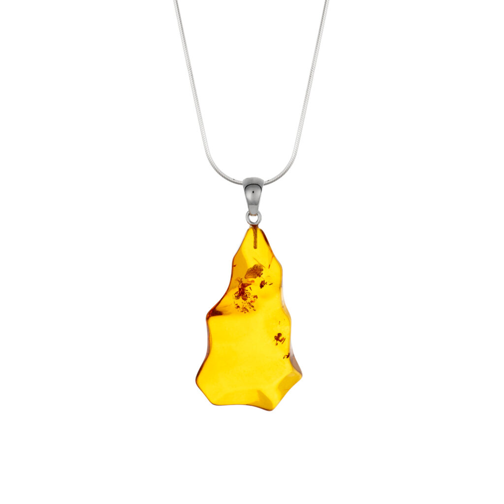 A close-up image of a genuine amber pendant showcasing its warm, golden hues. The amber is transparent with natural inclusions, capturing its organic beauty. The pendant is encased in a silver or gold frame, adding elegance to the raw, fossilized resin. The smooth surface of the amber reflects light, highlighting its natural glow and intricate details. This timeless piece of jewelry hangs delicately from a chain, blending nature and craftsmanship.