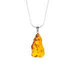 A close-up image of a genuine amber pendant showcasing its warm, golden hues. The amber is transparent with natural inclusions, capturing its organic beauty. The pendant is encased in a silver or gold frame, adding elegance to the raw, fossilized resin. The smooth surface of the amber reflects light, highlighting its natural glow and intricate details. This timeless piece of jewelry hangs delicately from a chain, blending nature and craftsmanship.