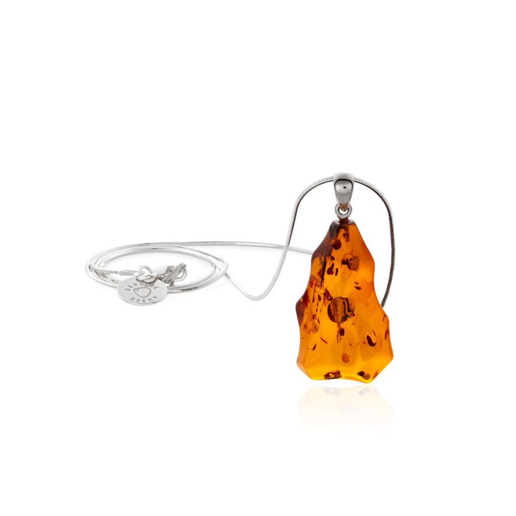 A close-up image of a genuine amber pendant showcasing its warm, golden hues. The amber is transparent with natural inclusions, capturing its organic beauty. The pendant is encased in a silver or gold frame, adding elegance to the raw, fossilized resin. The smooth surface of the amber reflects light, highlighting its natural glow and intricate details. This timeless piece of jewelry hangs delicately from a chain, blending nature and craftsmanship.