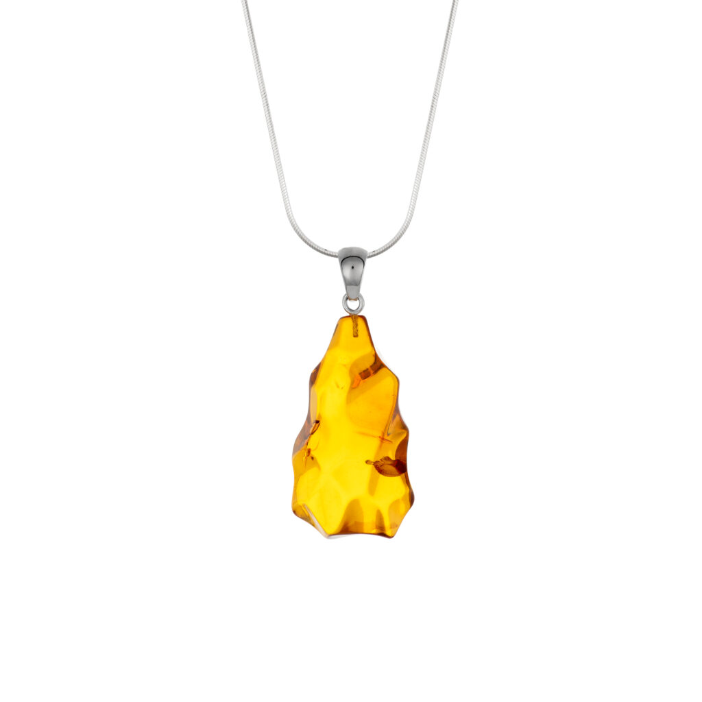 A close-up image of a genuine amber pendant showcasing its warm, golden hues. The amber is transparent with natural inclusions, capturing its organic beauty. The pendant is encased in a silver or gold frame, adding elegance to the raw, fossilized resin. The smooth surface of the amber reflects light, highlighting its natural glow and intricate details. This timeless piece of jewelry hangs delicately from a chain, blending nature and craftsmanship.