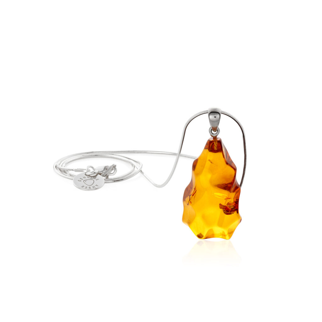 A close-up image of a genuine amber pendant showcasing its warm, golden hues. The amber is transparent with natural inclusions, capturing its organic beauty. The pendant is encased in a silver or gold frame, adding elegance to the raw, fossilized resin. The smooth surface of the amber reflects light, highlighting its natural glow and intricate details. This timeless piece of jewelry hangs delicately from a chain, blending nature and craftsmanship.