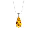 A close-up image of a genuine amber pendant showcasing its warm, golden hues. The amber is transparent with natural inclusions, capturing its organic beauty. The pendant is encased in a silver or gold frame, adding elegance to the raw, fossilized resin. The smooth surface of the amber reflects light, highlighting its natural glow and intricate details. This timeless piece of jewelry hangs delicately from a chain, blending nature and craftsmanship.