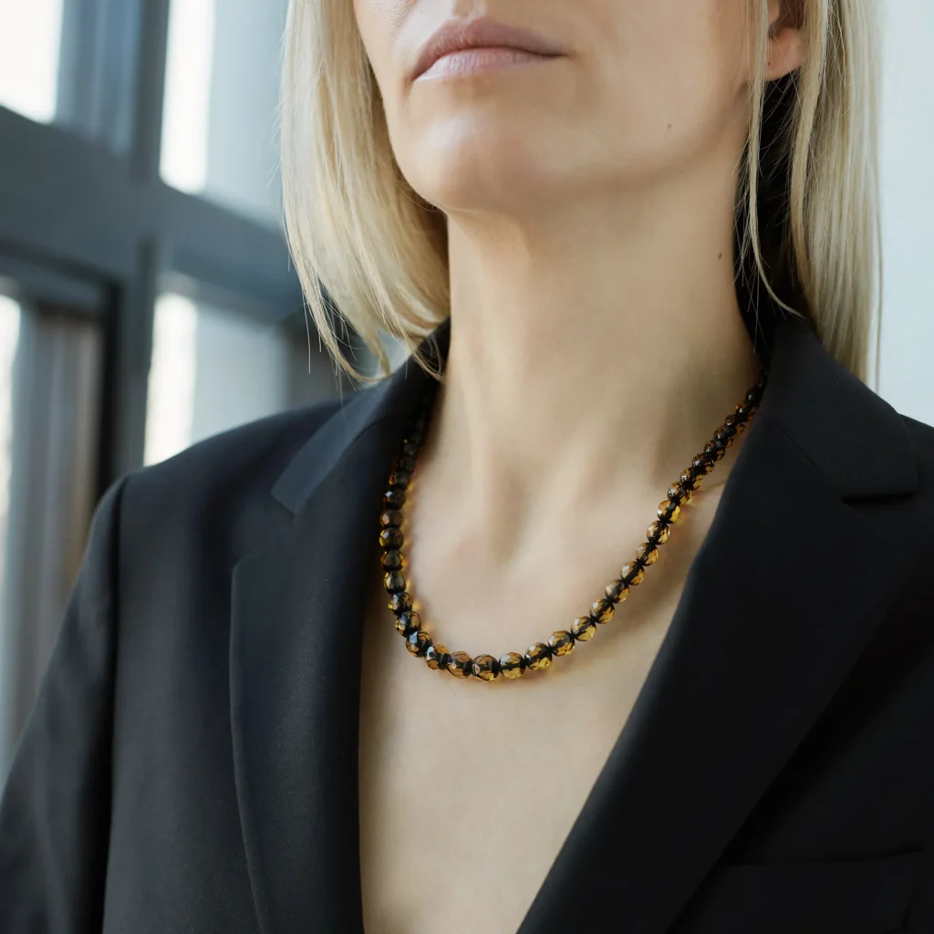 A close-up view of a genuine amber necklace, showcasing its warm, honey-colored beads. Each bead varies slightly in shade and transparency, with natural inclusions visible inside, adding to the necklace's unique charm. The necklace is strung on a delicate chain, highlighting the organic beauty of the amber stones.