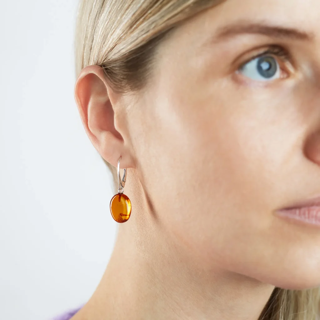 A pair of genuine amber earrings with translucent, warm golden-orange stones, showcasing natural inclusions. The amber is set in delicate silver or gold, highlighting its organic beauty. The earrings have a polished surface that reflects light, emphasizing the rich color variations and natural patterns within the amber. The earrings are lightweight, elegant, and exude a timeless, earthy charm, perfect for both casual and formal wear.