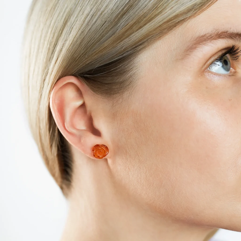 Close-up image of genuine cognac amber rose earrings, featuring warm, honey-brown amber stones intricately carved into the shape of roses. The translucent amber showcases natural inclusions, adding depth and character to the delicate floral design. Set in polished silver, these earrings blend the organic beauty of amber with the elegance of a rose motif.