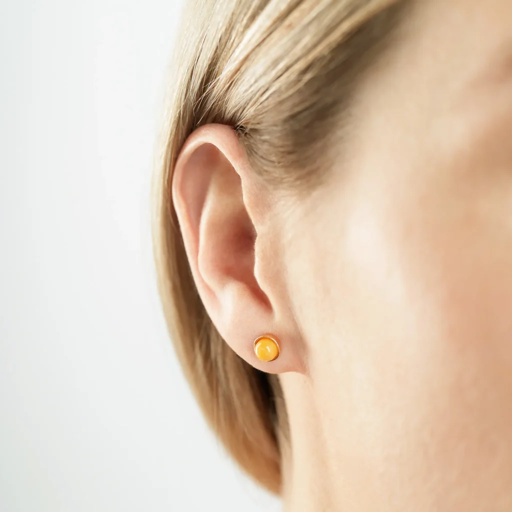 Close-up image of a pair of genuine amber earrings, showcasing their warm, golden-orange hue with natural inclusions. The earrings have a smooth, polished surface, highlighting the organic beauty of the amber, set in simple yet elegant silver clasps. The intricate details of the fossilized resin are visible, giving each piece a unique and timeless appeal.