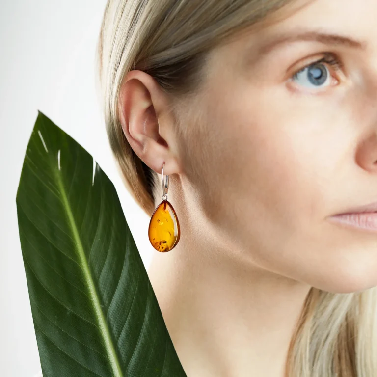 A pair of genuine amber earrings with translucent, warm golden-orange stones, showcasing natural inclusions. The amber is set in delicate silver or gold, highlighting its organic beauty. The earrings have a polished surface that reflects light, emphasizing the rich color variations and natural patterns within the amber. The earrings are lightweight, elegant, and exude a timeless, earthy charm, perfect for both casual and formal wear.