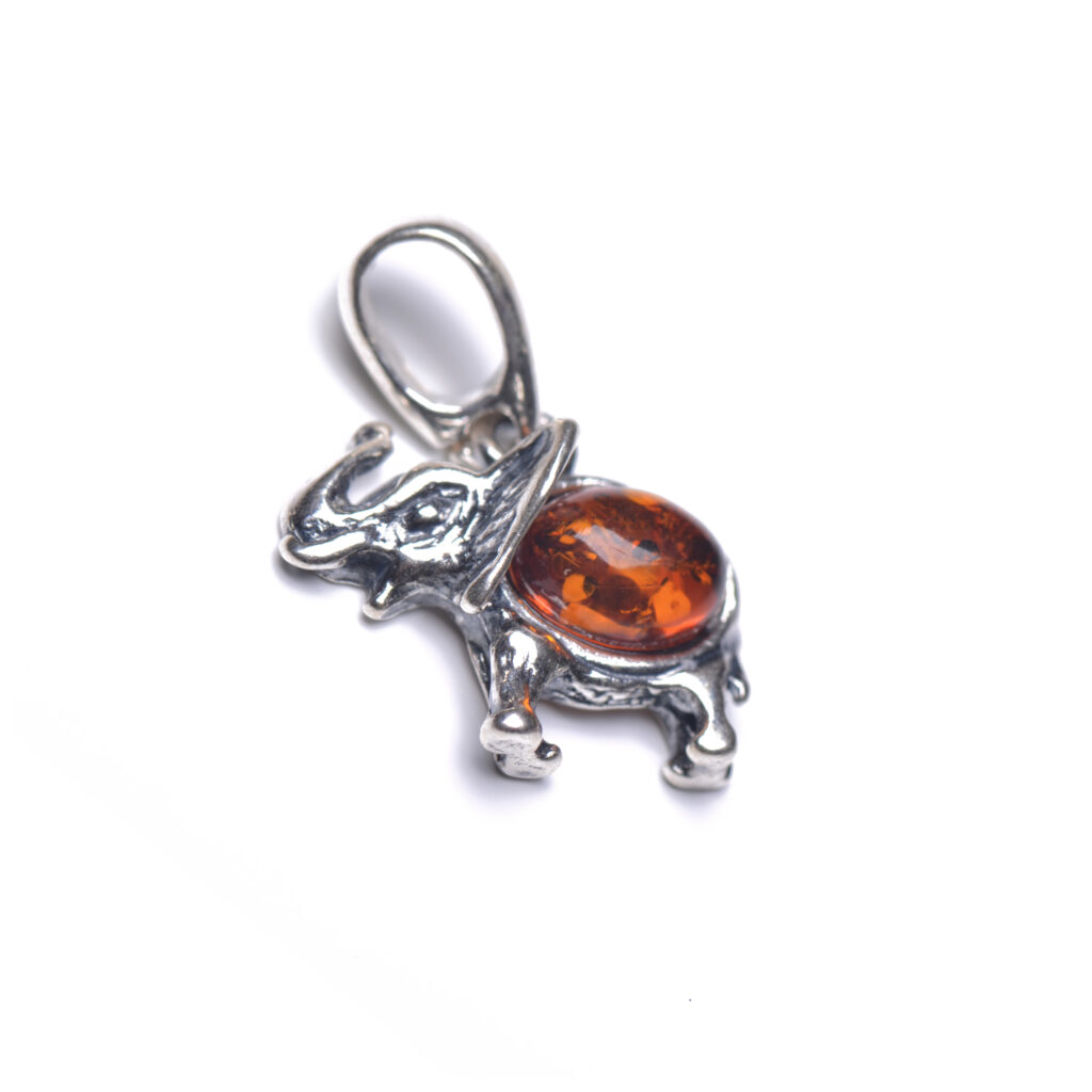 A detailed image of a genuine amber elephant pendant, featuring a smooth, warm amber body with natural inclusions. The elephant's shape is carefully crafted, with intricate details on the ears, trunk, and legs. The amber's golden hue contrasts beautifully with the silver or gold frame surrounding the pendant. The piece hangs gracefully from a chain, combining the symbolic strength of the elephant with the organic beauty of amber.