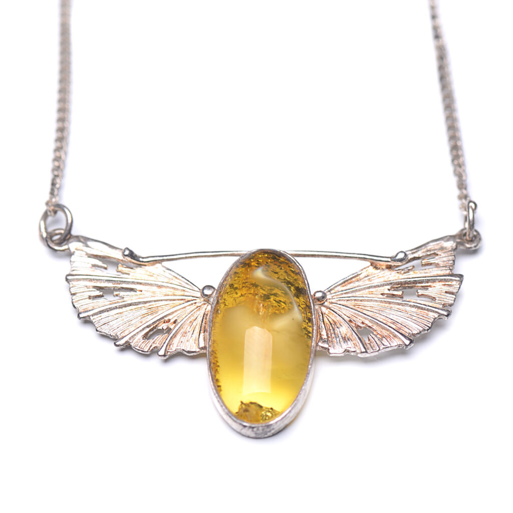 A close-up image of a genuine amber pendant showcasing its warm, golden hues. The amber is transparent with natural inclusions, capturing its organic beauty. The pendant is encased in a silver or gold frame, adding elegance to the raw, fossilized resin. The smooth surface of the amber reflects light, highlighting its natural glow and intricate details. This timeless piece of jewelry hangs delicately from a chain, blending nature and craftsmanship.