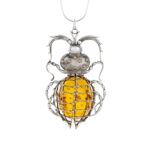 A close-up image of an exclusive collector's item: a sterling silver and gold beetle pendant featuring a large, genuine amber piece. The beetle's body is intricately crafted with silver and gold details, giving it a lifelike appearance. The centerpiece is a striking, polished amber stone, rich with warm, golden hues and natural inclusions, seamlessly set into the beetle's back. The craftsmanship blends luxury and nature, making it a rare and elegant piece of wearable art.