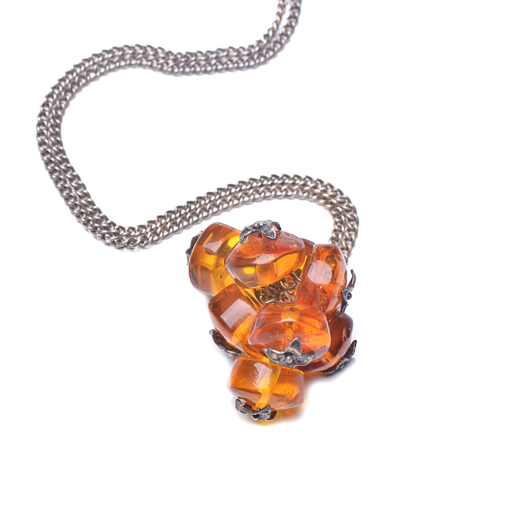 A close-up image of a genuine amber pendant showcasing its warm, golden hues. The amber is transparent with natural inclusions, capturing its organic beauty. The pendant is encased in a silver or gold frame, adding elegance to the raw, fossilized resin. The smooth surface of the amber reflects light, highlighting its natural glow and intricate details. This timeless piece of jewelry hangs delicately from a chain, blending nature and craftsmanship.