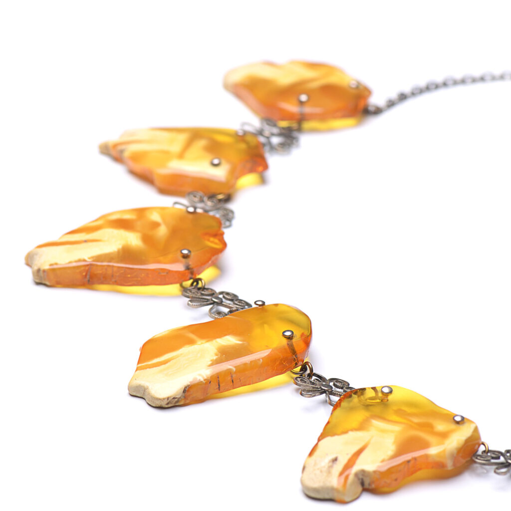 A close-up image of a genuine amber necklace, featuring smooth, polished amber beads. The beads vary slightly in size and shape, showcasing their natural organic origins. The necklace is elegantly strung together with a subtle clasp, highlighting the translucent and rich tones of the amber. The warm glow of the amber stones contrasts beautifully against the background, giving the piece a timeless and earthy appeal.