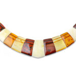 A close-up image of a genuine amber necklace, featuring smooth, polished amber beads. The beads vary slightly in size and shape, showcasing their natural organic origins. The necklace is elegantly strung together with a subtle clasp, highlighting the translucent and rich tones of the amber. The warm glow of the amber stones contrasts beautifully against the background, giving the piece a timeless and earthy appeal.