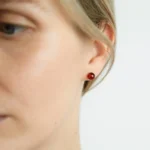 Close-up of a red Baltic amber stud earring on a persons ear.