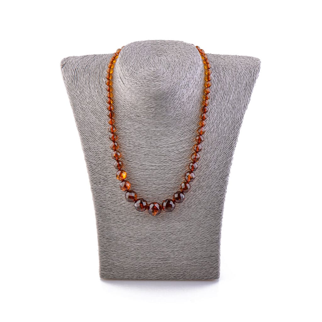 Handmade Baltic amber necklace with varied cognac beads on a gray bust display.