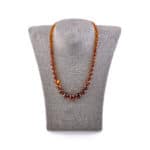 Handmade Baltic amber necklace with varied cognac beads on a gray bust display.