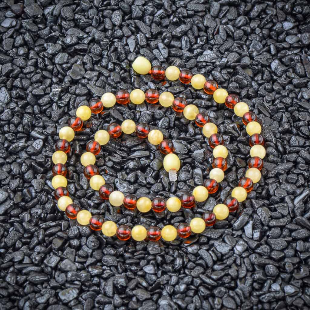 Vibrant amber beaded necklace arranged in a circular pattern against dark pebbles background.