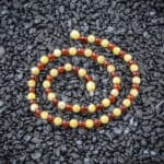 Vibrant amber beaded necklace arranged in a circular pattern against dark pebbles background.