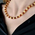 Elegant Baltic amber necklace with warm, dual-tone beads worn over a black blouse.